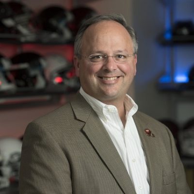 Man with glasses wearing a white collared shirt and tannish, plaid jacket