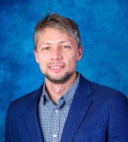 Image of Oleg Kim, blue suit jacket and small-checkered blue and white shirt